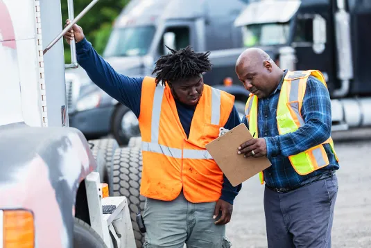 Two truckers talking and looking at a clipboard. 