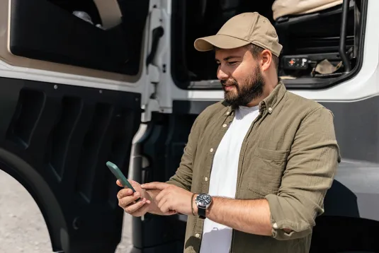 Truck driver standing by truck and looking at a phone. 