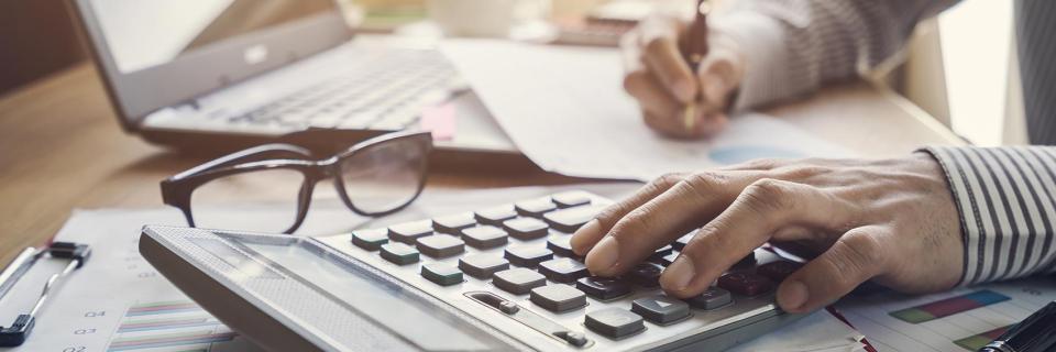 person typing on calculator next to computer